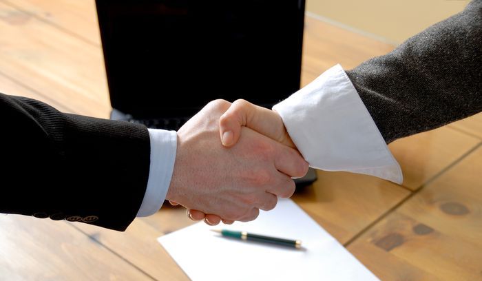 man and woman shaking hands in front of laptop